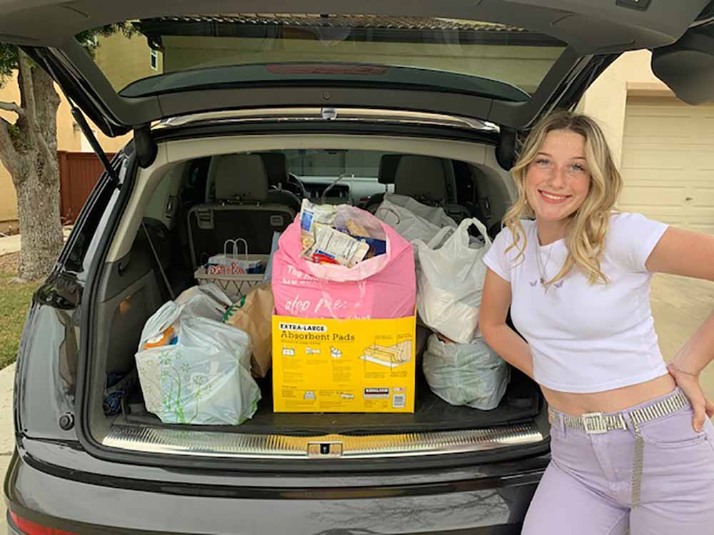 Picture of Chloe in front of her car with donated items collected for the less fortunate!