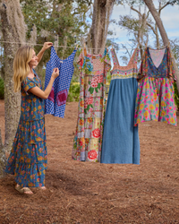 Woman hanging colorful dresses on a clothesline outdoors.