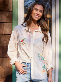 Woman wearing a white blouse with floral embroidery standing outdoors.