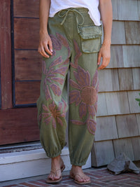 Person wearing green floral-patterned pants standing in front of a wooden door.