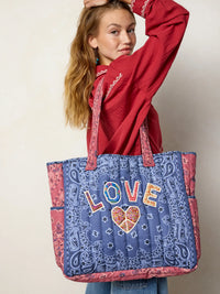 Woman holding a blue tote bag with 'LOVE' and heart design, wearing a red sweatshirt.