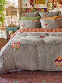 Patchwork bedspread with floral embroidery on a bed in a decorated room.