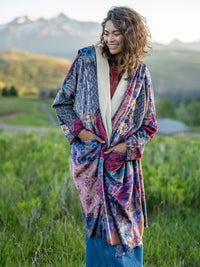 Woman wearing a colorful patterned kimono standing in a grassy field with mountains in the background