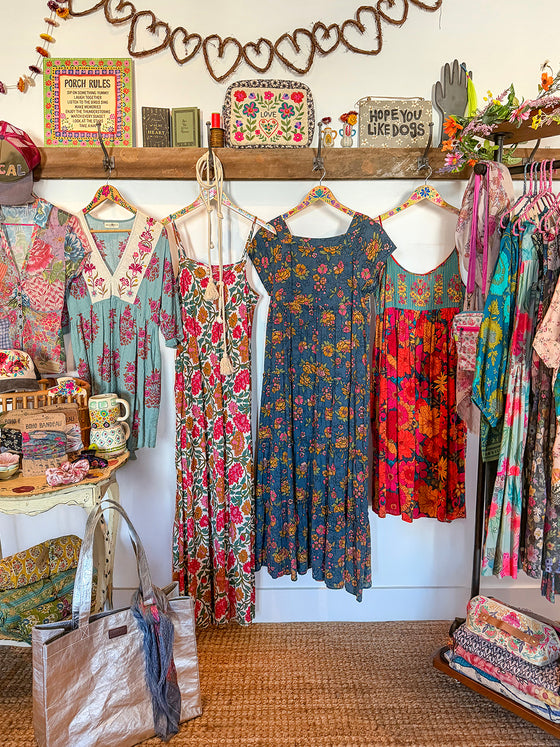 Colorful vintage dresses hanging on a rack in a store with decorative elements.