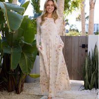 Woman in a floral dress standing outdoors with plants and a wooden gate in the background