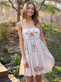 Woman wearing a floral embroidered dress standing outdoors in a natural setting.