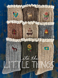 Nine knitted socks arranged in a 3x3 grid on a distressed blue wooden background, each with a different embroidered winter-themed motif and cream ruffle trim. Large white text at the bottom reads 'it's the LITTLE THINGS'.