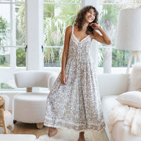 Woman in a white lace dress standing in a bright living room with large windows.
