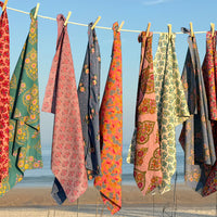 Colorful patterned sheets hanging on a clothesline with a clear blue sky in the background.