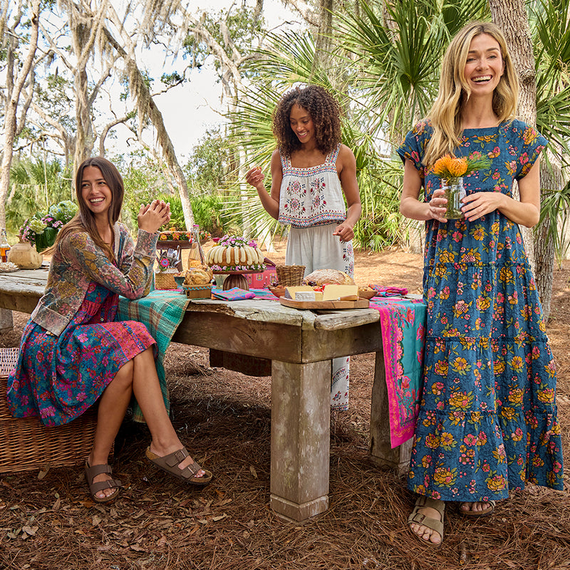 Three women sitting around a wooden table outdoors, enjoying a picnic.