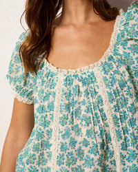 Close-up of a floral top with lace details on a plain background