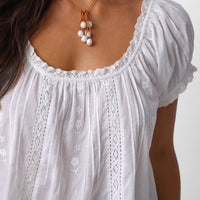 White lace-trimmed blouse with a necklace on a plain background