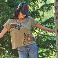 girl in a hat and green tee shirt with bears and a cabin on it in the woods