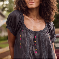 girl in a black embroidered blouse in front of a fence